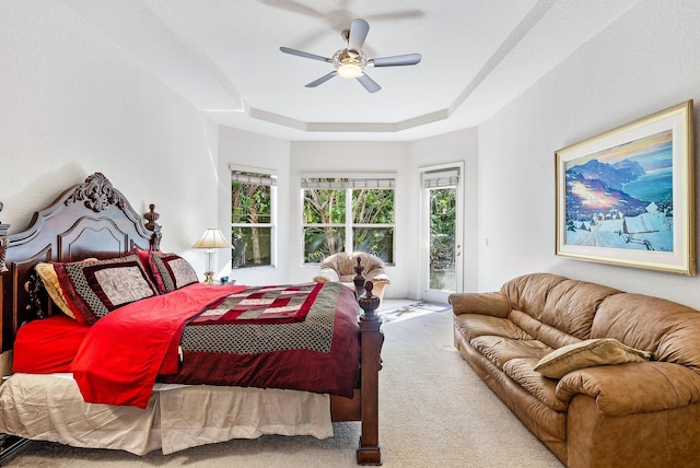 bedroom with access to outside, ceiling fan, a tray ceiling, and carpet