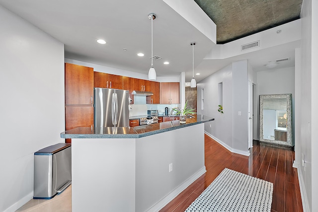 kitchen featuring hanging light fixtures, hardwood / wood-style flooring, stainless steel fridge, and decorative backsplash