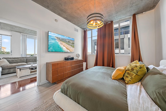 bedroom featuring an inviting chandelier, multiple windows, visible vents, and light wood finished floors