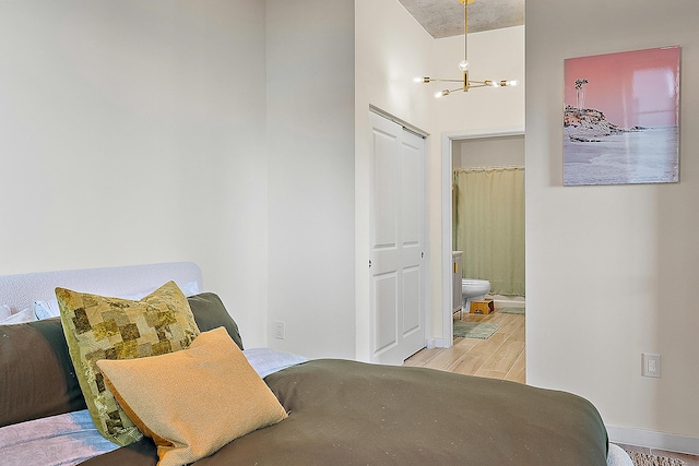 bedroom with a notable chandelier, connected bathroom, and light wood-type flooring