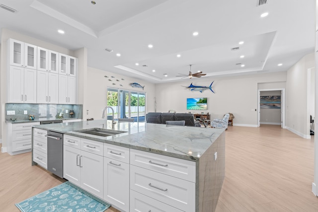 kitchen with white cabinets, light wood-type flooring, a tray ceiling, and a kitchen island with sink