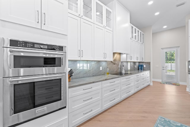 kitchen featuring light stone countertops, light wood-type flooring, stainless steel double oven, black electric cooktop, and white cabinetry