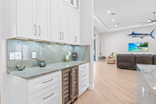 kitchen featuring light stone countertops, white cabinetry, beverage cooler, and light hardwood / wood-style floors