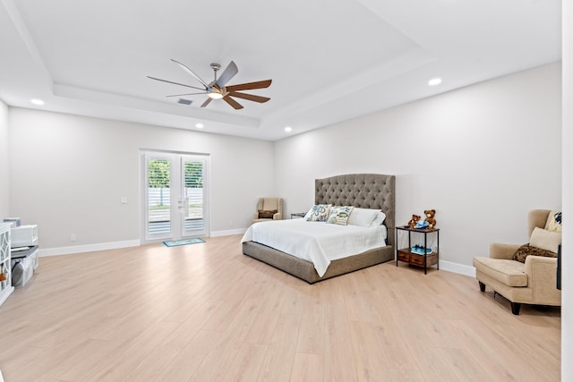 bedroom with access to exterior, light hardwood / wood-style floors, ceiling fan, and a tray ceiling