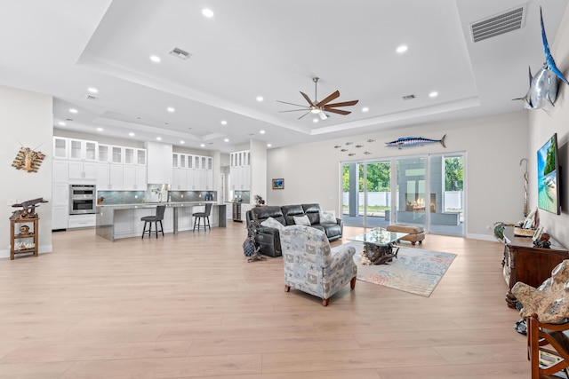 living room with light hardwood / wood-style floors, a raised ceiling, ceiling fan, and sink