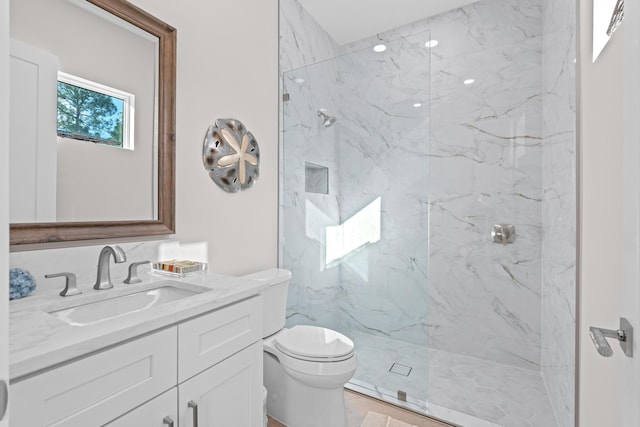 bathroom with a tile shower, vanity, and toilet