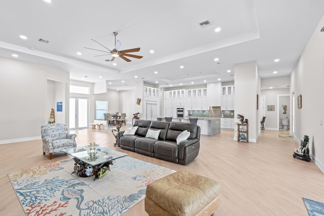 living room with ceiling fan, a tray ceiling, and light hardwood / wood-style flooring