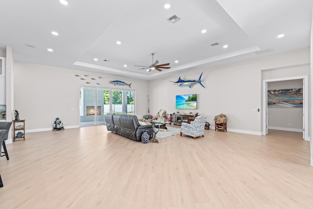 living room with a raised ceiling, light hardwood / wood-style flooring, and ceiling fan