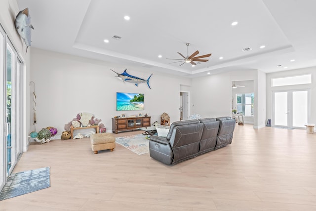 living room with french doors, light hardwood / wood-style floors, a raised ceiling, and ceiling fan