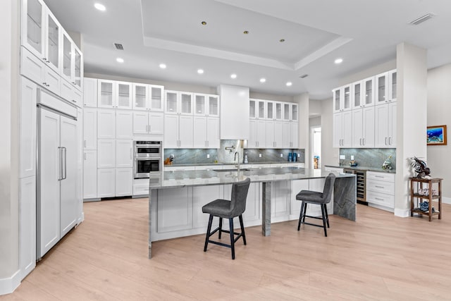 kitchen featuring a raised ceiling, a center island with sink, white cabinetry, and a breakfast bar area