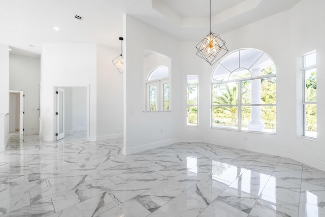 empty room with plenty of natural light, a high ceiling, and an inviting chandelier