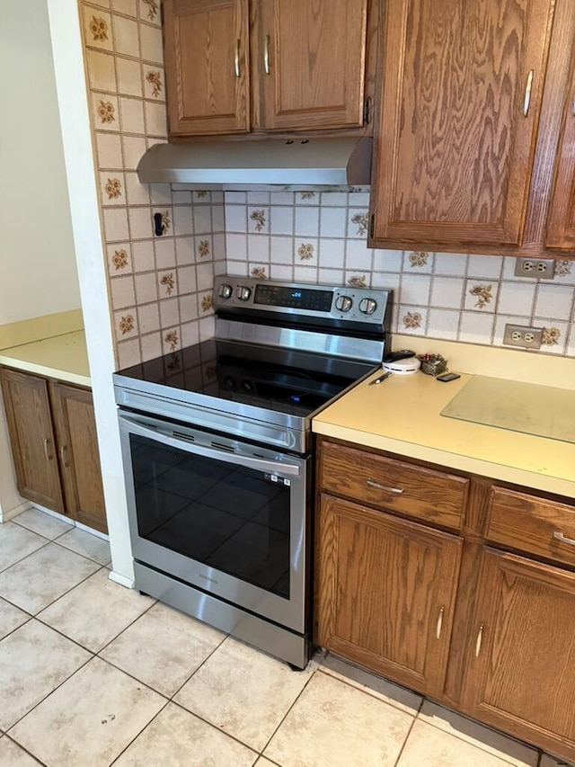 kitchen featuring stainless steel range with electric stovetop, tasteful backsplash, under cabinet range hood, and light tile patterned floors