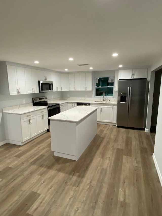 kitchen with light stone countertops, stainless steel appliances, white cabinets, a kitchen island, and light wood-type flooring