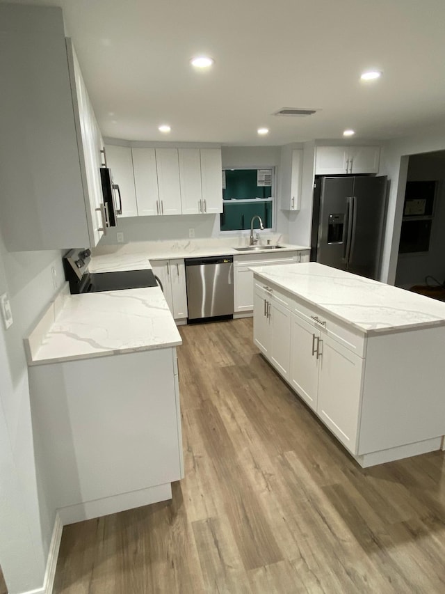 kitchen with light stone countertops, appliances with stainless steel finishes, light wood-type flooring, a kitchen island, and white cabinetry