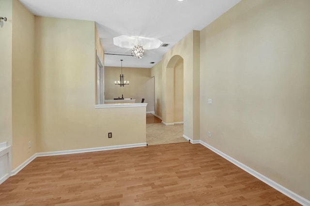 spare room featuring a chandelier and light wood-type flooring