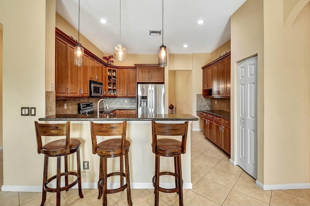 kitchen with kitchen peninsula, dark stone counters, decorative light fixtures, decorative backsplash, and appliances with stainless steel finishes