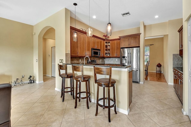 kitchen featuring backsplash, dark stone countertops, decorative light fixtures, kitchen peninsula, and stainless steel appliances