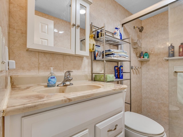 bathroom with a tile shower, a textured ceiling, toilet, vanity, and tile walls