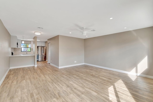 unfurnished living room featuring light hardwood / wood-style floors, ceiling fan, and sink