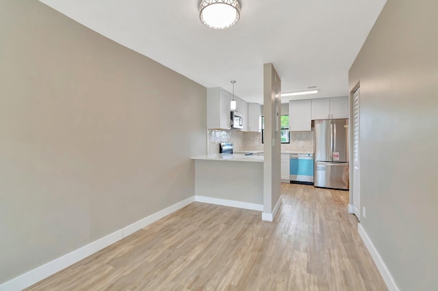 kitchen featuring kitchen peninsula, stainless steel appliances, pendant lighting, light hardwood / wood-style flooring, and white cabinetry