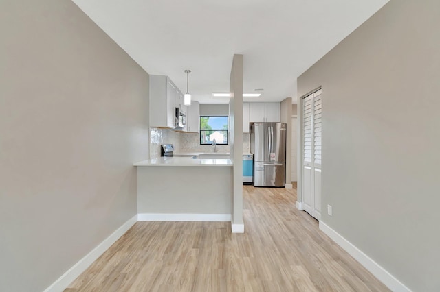 kitchen featuring kitchen peninsula, appliances with stainless steel finishes, pendant lighting, white cabinets, and light wood-type flooring