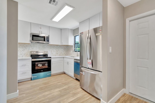 kitchen featuring decorative backsplash, appliances with stainless steel finishes, sink, light hardwood / wood-style floors, and white cabinetry