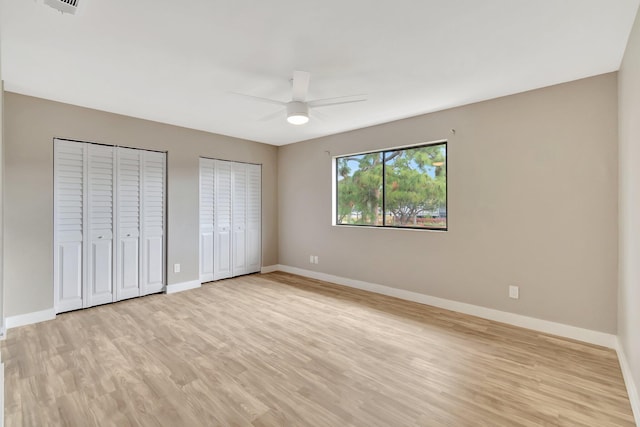 unfurnished bedroom with ceiling fan, light hardwood / wood-style flooring, and two closets