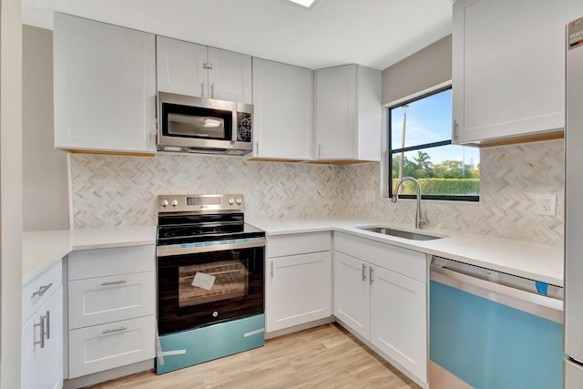 kitchen featuring light wood-type flooring, backsplash, stainless steel appliances, sink, and white cabinets