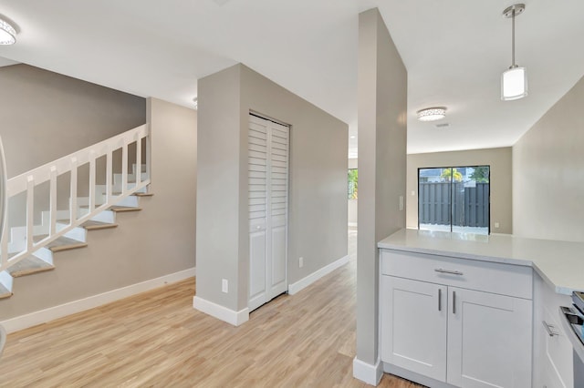 kitchen with white cabinets, light hardwood / wood-style floors, hanging light fixtures, and stainless steel stove