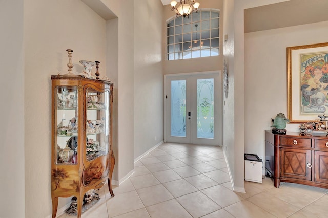 tiled entrance foyer with french doors, a high ceiling, and a notable chandelier