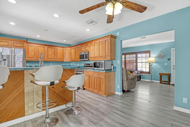 kitchen with ceiling fan, light wood-type flooring, a breakfast bar area, and appliances with stainless steel finishes