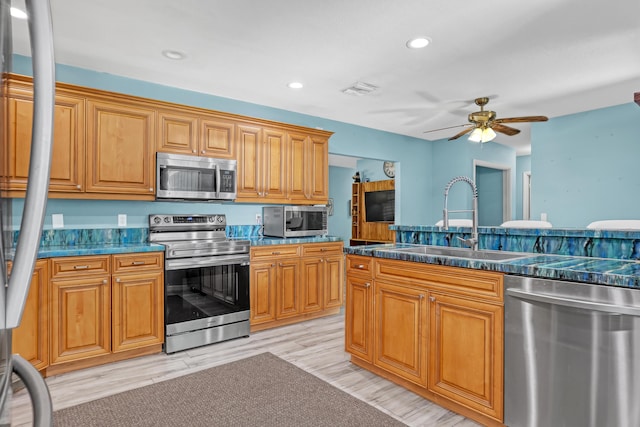 kitchen featuring appliances with stainless steel finishes, light wood-type flooring, ceiling fan, and sink