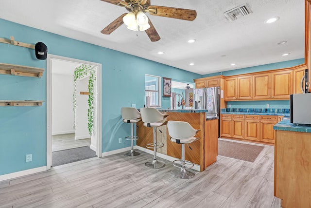 kitchen featuring ceiling fan, sink, a breakfast bar area, appliances with stainless steel finishes, and light wood-type flooring