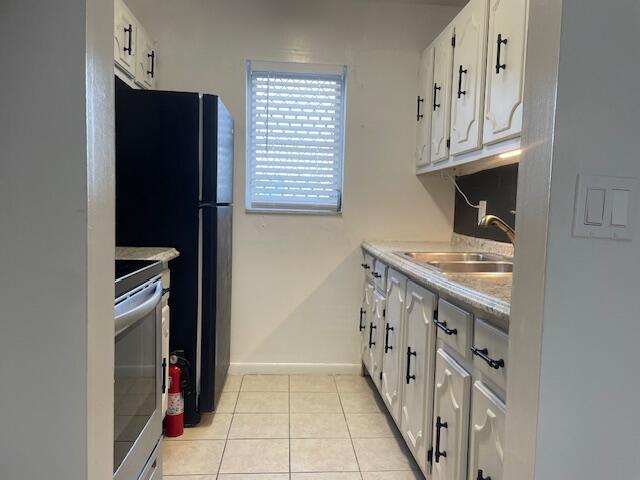 kitchen featuring sink, light tile patterned floors, white cabinets, range, and fridge