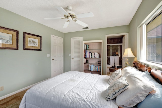 bedroom with ceiling fan, ensuite bathroom, carpet floors, and a textured ceiling