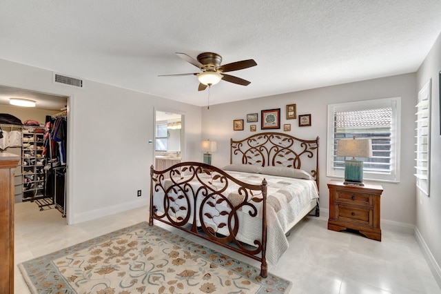 bedroom with a textured ceiling, a walk in closet, a closet, and ceiling fan