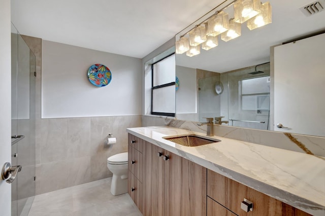 bathroom featuring tiled shower, vanity, toilet, and tile walls