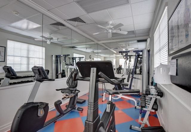 exercise room featuring a paneled ceiling, ceiling fan, and plenty of natural light