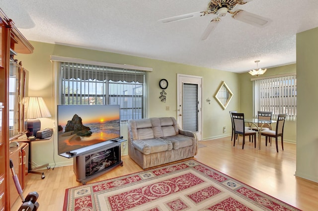 living room featuring a textured ceiling, ceiling fan with notable chandelier, and light hardwood / wood-style floors