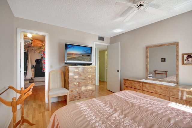 bedroom with a spacious closet, ceiling fan, light hardwood / wood-style floors, a textured ceiling, and a closet