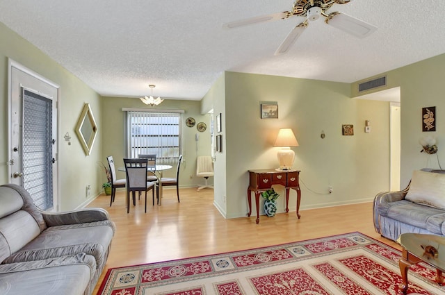 living room with a textured ceiling, light hardwood / wood-style floors, and ceiling fan with notable chandelier