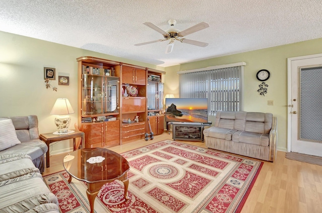 living room featuring ceiling fan, light hardwood / wood-style flooring, and a textured ceiling