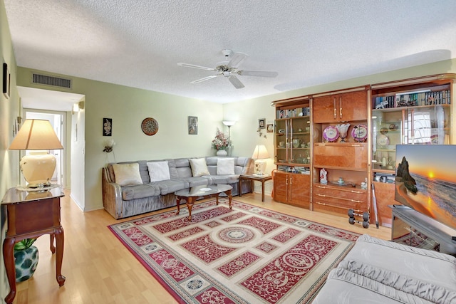 living room featuring ceiling fan, a textured ceiling, and light hardwood / wood-style flooring