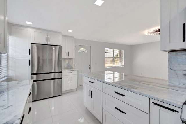 kitchen with white cabinets, stainless steel fridge, tasteful backsplash, and light stone counters