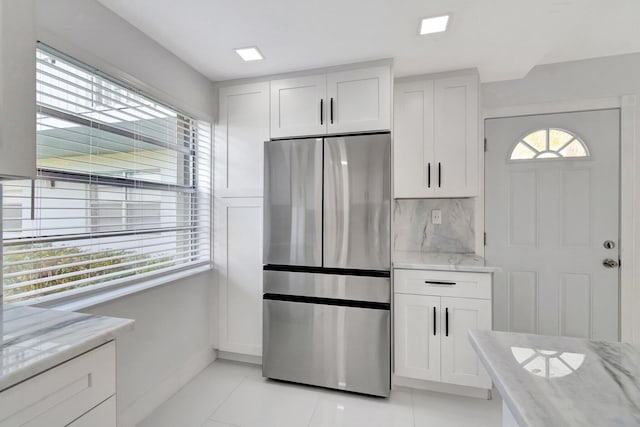 kitchen featuring stainless steel fridge, white cabinetry, and light stone counters