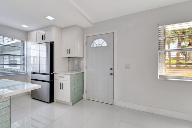 kitchen with stainless steel fridge, light tile patterned floors, white cabinetry, and a wealth of natural light