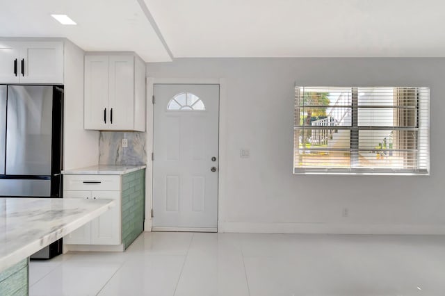 kitchen with stainless steel refrigerator, white cabinetry, light stone counters, backsplash, and light tile patterned floors