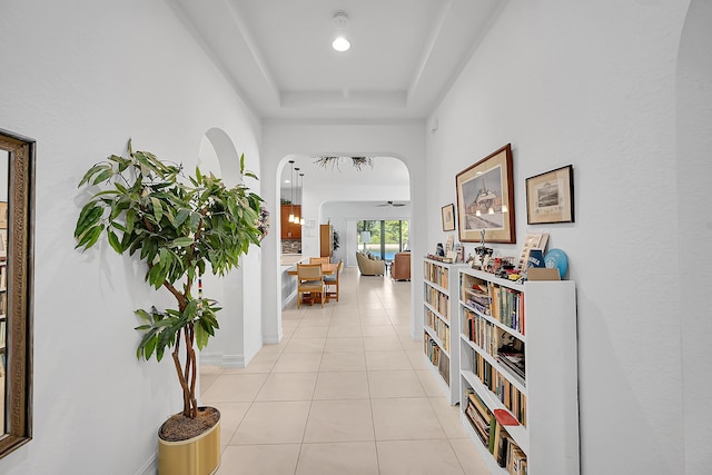 hall featuring light tile patterned floors and a tray ceiling