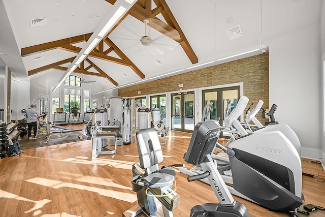 gym with ceiling fan, french doors, high vaulted ceiling, brick wall, and hardwood / wood-style floors