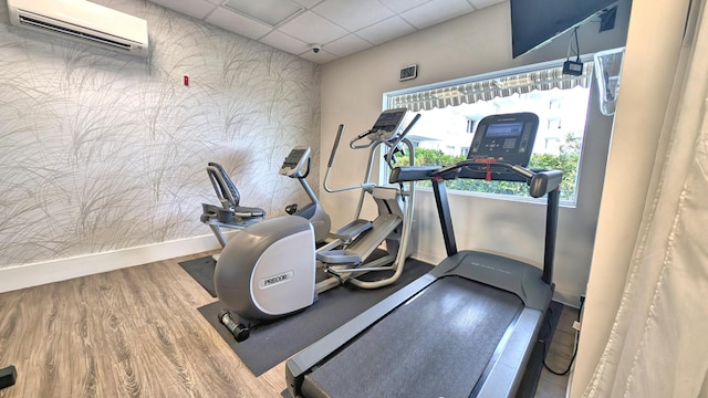 workout area with hardwood / wood-style flooring, a wall unit AC, and a drop ceiling